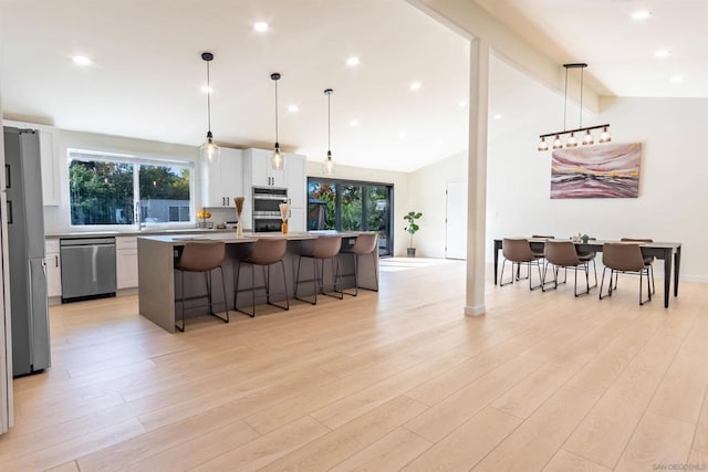 kitchen with stainless steel appliances, white cabinets, vaulted ceiling with beams, hanging light fixtures, and a kitchen island with sink