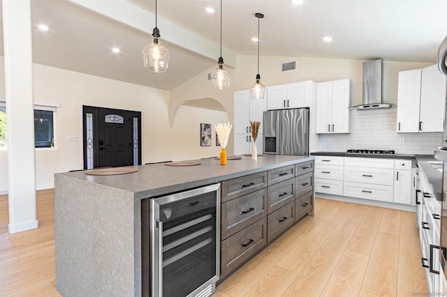 kitchen with white cabinets, a center island, stainless steel fridge, wall chimney range hood, and wine cooler