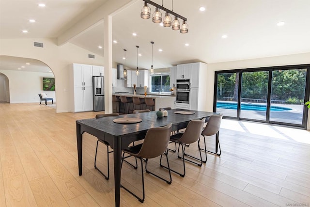 dining area featuring light wood-type flooring and vaulted ceiling with beams