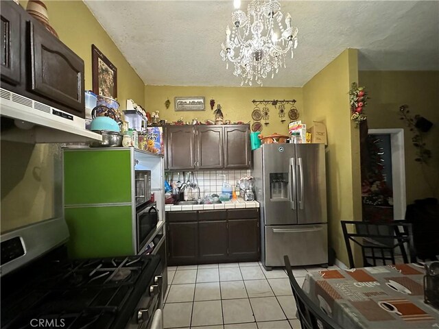 kitchen featuring tile counters, decorative light fixtures, appliances with stainless steel finishes, a notable chandelier, and dark brown cabinets