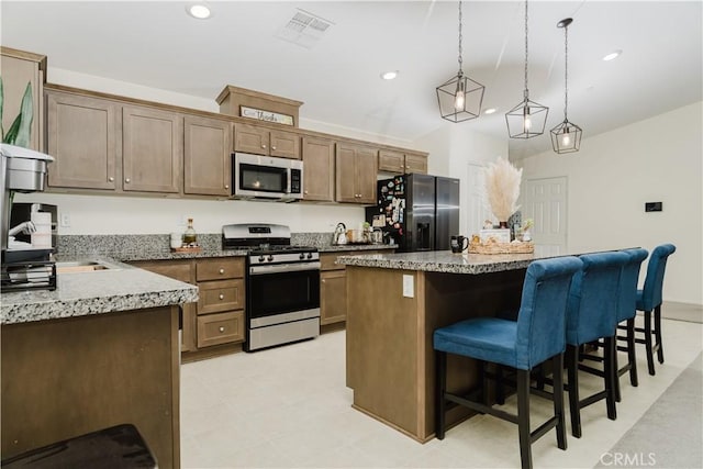 kitchen with light stone countertops, pendant lighting, a kitchen bar, a kitchen island, and appliances with stainless steel finishes