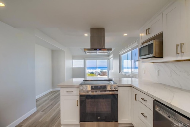 kitchen with kitchen peninsula, island range hood, white cabinets, and stainless steel appliances