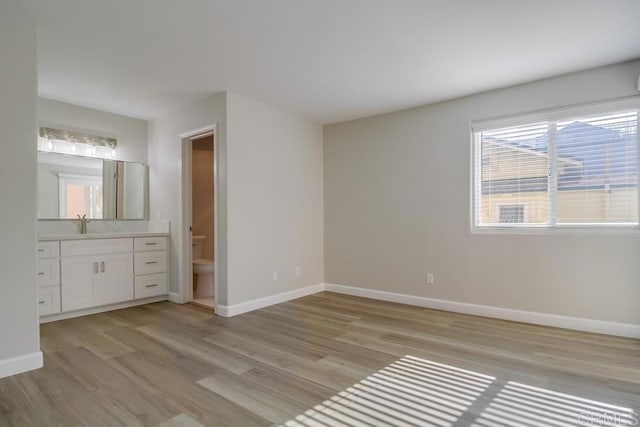 unfurnished bedroom featuring connected bathroom, sink, and light wood-type flooring