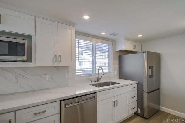 kitchen with decorative backsplash, appliances with stainless steel finishes, light stone countertops, sink, and white cabinets