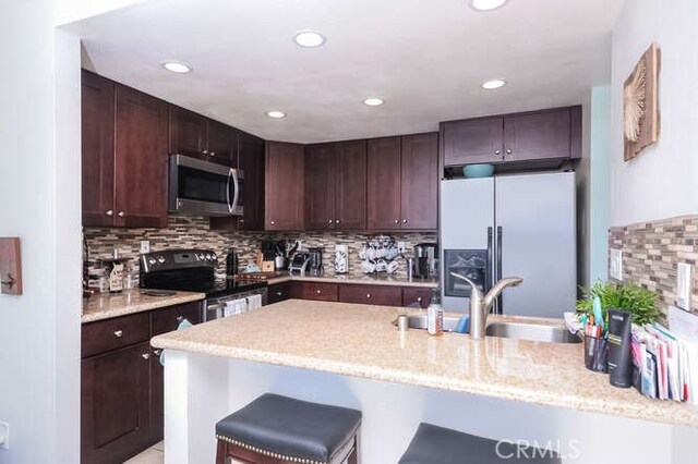 kitchen with sink, dark brown cabinets, a kitchen breakfast bar, and appliances with stainless steel finishes