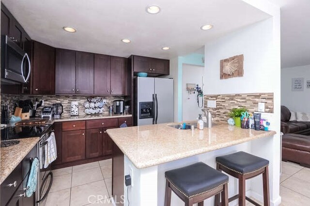 kitchen with light tile patterned flooring, a breakfast bar area, tasteful backsplash, appliances with stainless steel finishes, and a kitchen island with sink