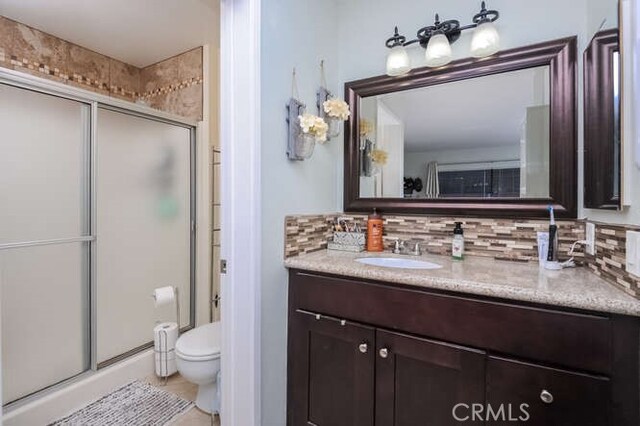 bathroom featuring a shower with door, vanity, backsplash, and toilet