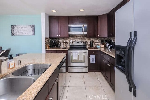 kitchen featuring tasteful backsplash, sink, light tile patterned floors, light stone counters, and stainless steel appliances