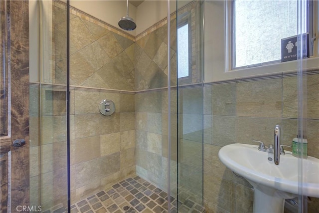 bathroom featuring a tile shower, sink, and tile walls