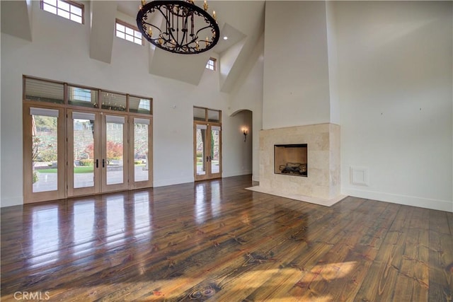 unfurnished living room featuring plenty of natural light, dark hardwood / wood-style flooring, a towering ceiling, and french doors