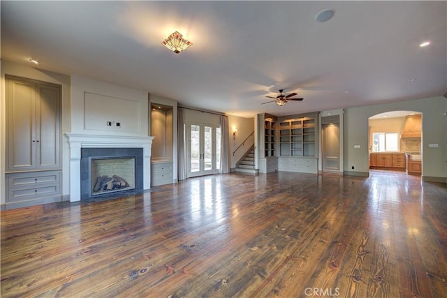 unfurnished living room with a tiled fireplace, ceiling fan, dark wood-type flooring, and a healthy amount of sunlight