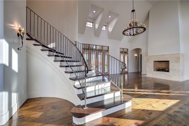 stairway with a towering ceiling, hardwood / wood-style flooring, a notable chandelier, and a tiled fireplace