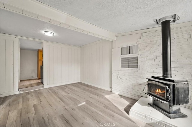 unfurnished living room featuring a wood stove, a textured ceiling, and light hardwood / wood-style flooring