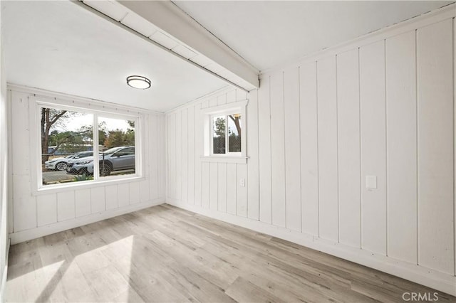 empty room featuring wood walls, light hardwood / wood-style flooring, and lofted ceiling with beams