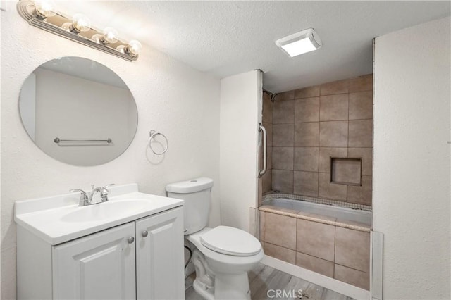 full bathroom featuring a textured ceiling, vanity, toilet, and tiled shower / bath