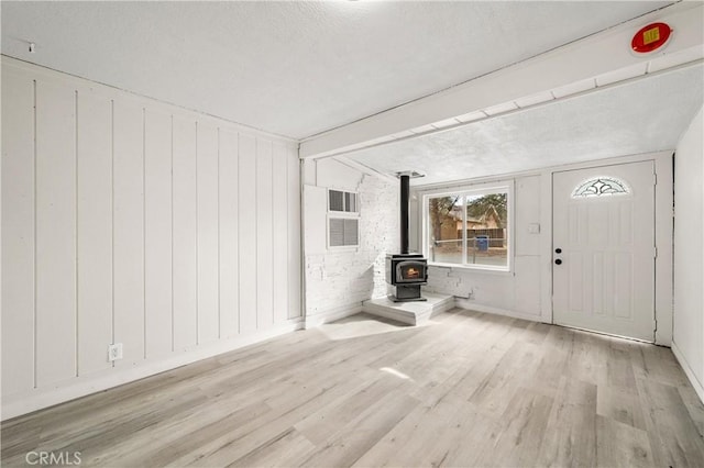 foyer with a wood stove, a textured ceiling, brick wall, and light hardwood / wood-style flooring