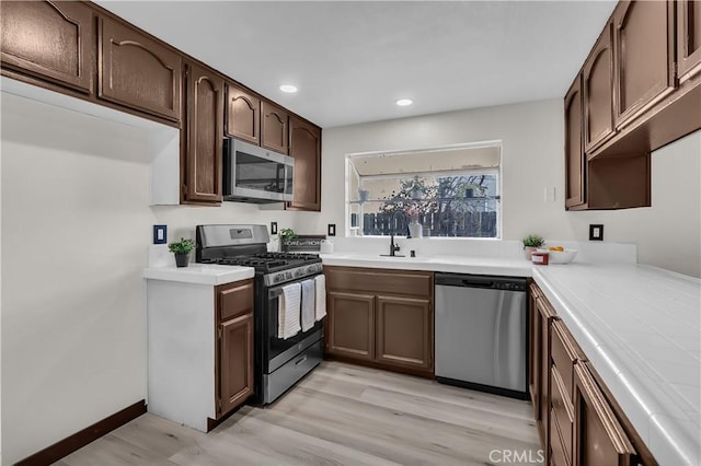 kitchen with appliances with stainless steel finishes, sink, dark brown cabinetry, and light hardwood / wood-style flooring