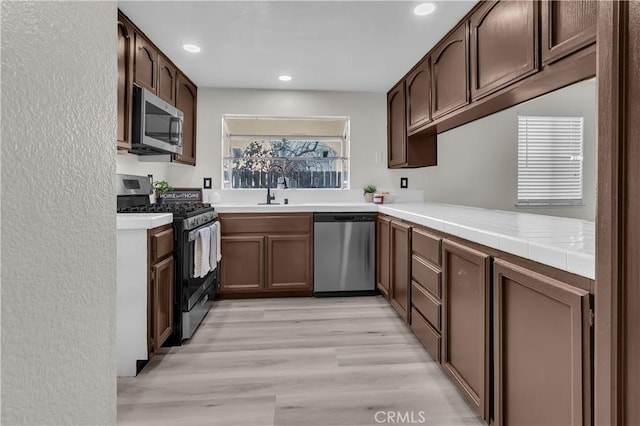 kitchen featuring sink, tile countertops, light hardwood / wood-style flooring, appliances with stainless steel finishes, and kitchen peninsula