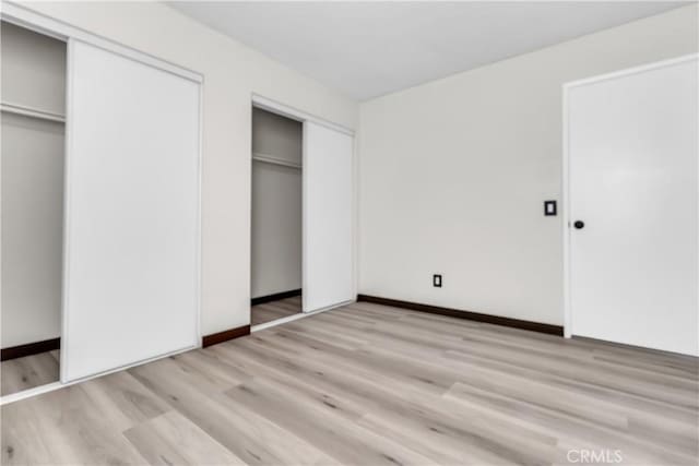 unfurnished bedroom featuring two closets and light hardwood / wood-style flooring