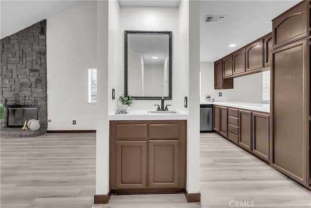 kitchen with sink, light hardwood / wood-style flooring, dishwasher, dark brown cabinets, and a fireplace