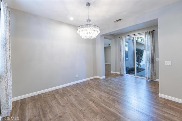 unfurnished room featuring an inviting chandelier and hardwood / wood-style floors