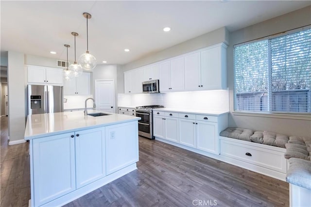 kitchen with appliances with stainless steel finishes, decorative light fixtures, white cabinetry, an island with sink, and sink