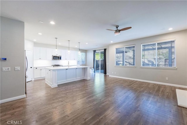 kitchen with pendant lighting, white cabinetry, wood-type flooring, and a center island with sink