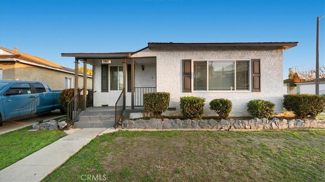 bungalow-style house with a porch, a front lawn, and stucco siding