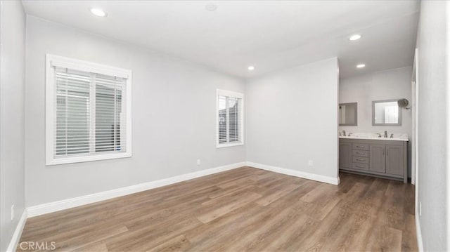 unfurnished bedroom featuring recessed lighting, a sink, baseboards, light wood-style floors, and ensuite bath