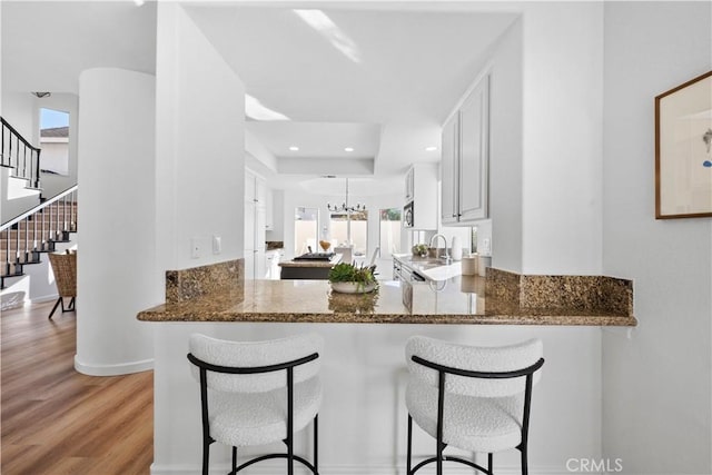 kitchen with kitchen peninsula, white cabinetry, light hardwood / wood-style flooring, and dark stone counters