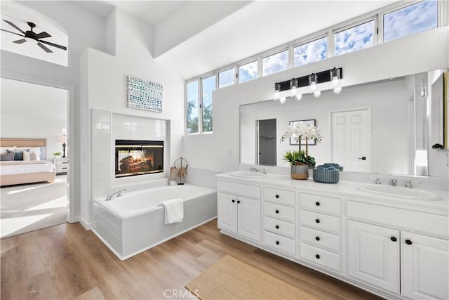 bathroom featuring vanity, a multi sided fireplace, hardwood / wood-style flooring, ceiling fan, and a towering ceiling