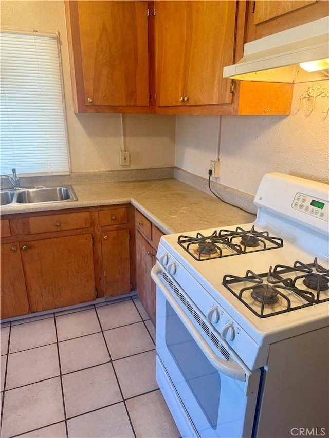 kitchen with light tile patterned floors, white gas range oven, and sink