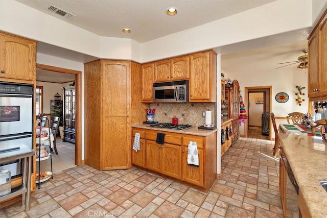 kitchen featuring backsplash, stainless steel appliances, light stone counters, and ceiling fan