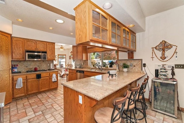 kitchen with a kitchen breakfast bar, ceiling fan, appliances with stainless steel finishes, light stone counters, and kitchen peninsula