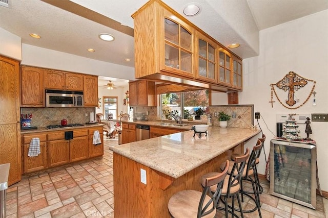 19985 Red Feather Rd, Apple Valley, CA 92307 - kitchen with appliances with stainless steel finishes, brown cabinetry, decorative backsplash, glass insert cabinets, and a peninsula