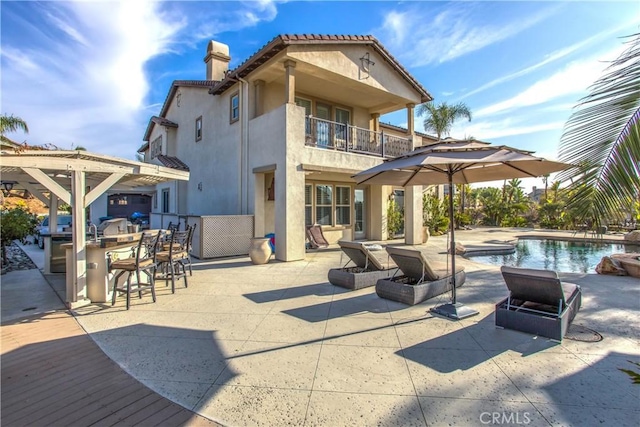 back of house with exterior kitchen, a balcony, an outdoor bar, and a patio