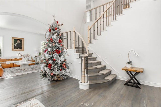 staircase featuring wood-type flooring, a towering ceiling, and crown molding