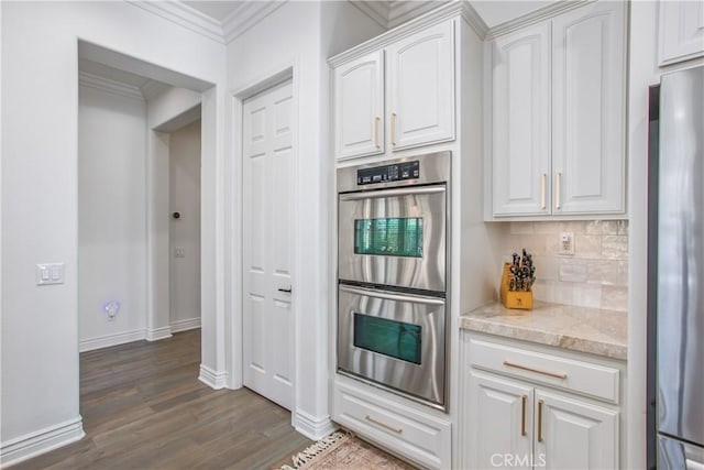 kitchen with appliances with stainless steel finishes, dark hardwood / wood-style flooring, white cabinetry, and ornamental molding