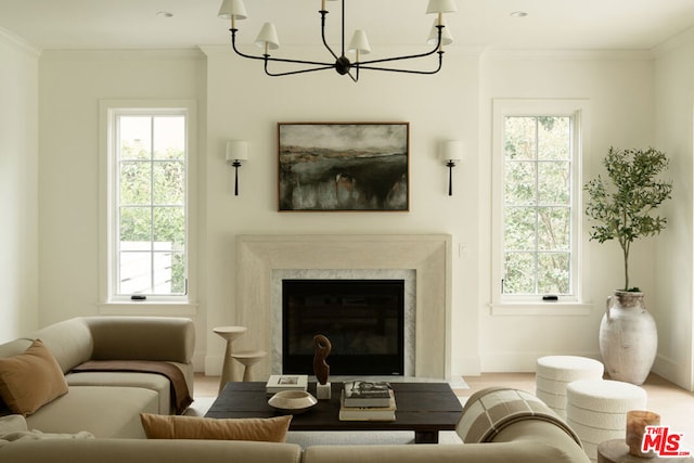 living area featuring a wealth of natural light, a premium fireplace, a notable chandelier, and ornamental molding