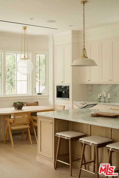 kitchen featuring breakfast area, hanging light fixtures, light wood-type flooring, black oven, and a breakfast bar area