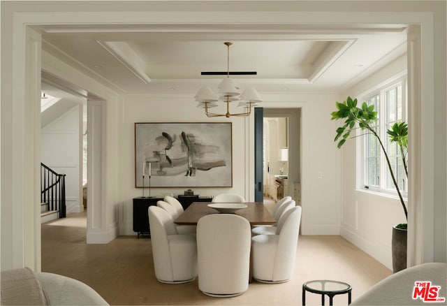 dining area with an inviting chandelier, light wood-type flooring, ornamental molding, and a tray ceiling