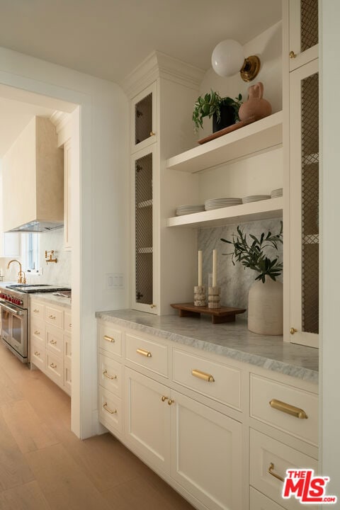 bar featuring tasteful backsplash, white cabinetry, high end stainless steel range, and wall chimney range hood