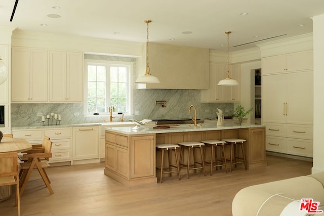 kitchen featuring decorative backsplash, a kitchen island with sink, hanging light fixtures, and light wood-type flooring