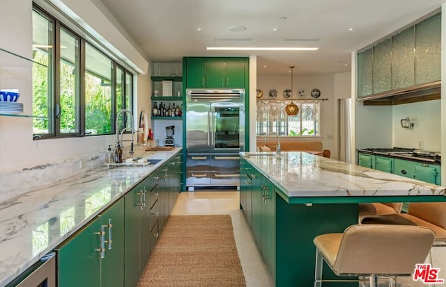 kitchen featuring sink, a kitchen breakfast bar, green cabinets, light stone counters, and a kitchen island