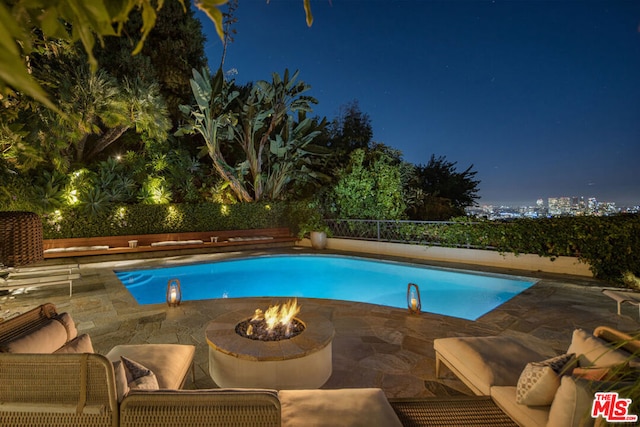 pool at night featuring a patio area and an outdoor fire pit