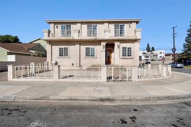 view of front of home with a balcony, a gate, a fenced front yard, and stucco siding