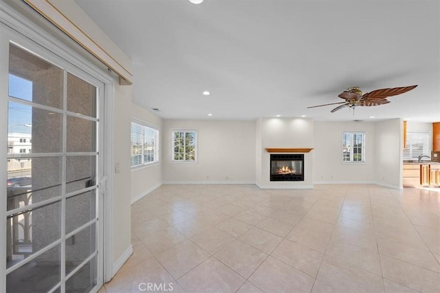 unfurnished living room with a ceiling fan, baseboards, recessed lighting, a sink, and a glass covered fireplace