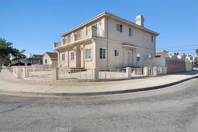 view of front of house featuring stucco siding, a balcony, a fenced front yard, and a chimney