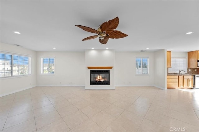 unfurnished living room featuring a sink, a glass covered fireplace, recessed lighting, light tile patterned floors, and baseboards