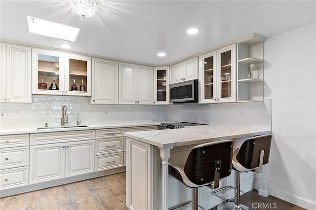 kitchen with a kitchen breakfast bar, sink, light hardwood / wood-style flooring, light stone counters, and white cabinetry